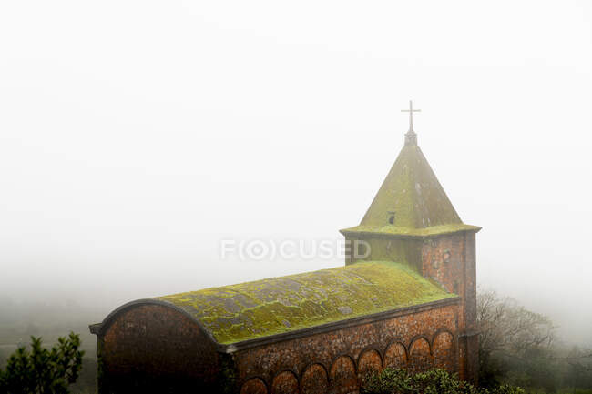 Antigua capilla de ladrillo con musgo verde en el techo en la niebla espesa, Camboya - foto de stock