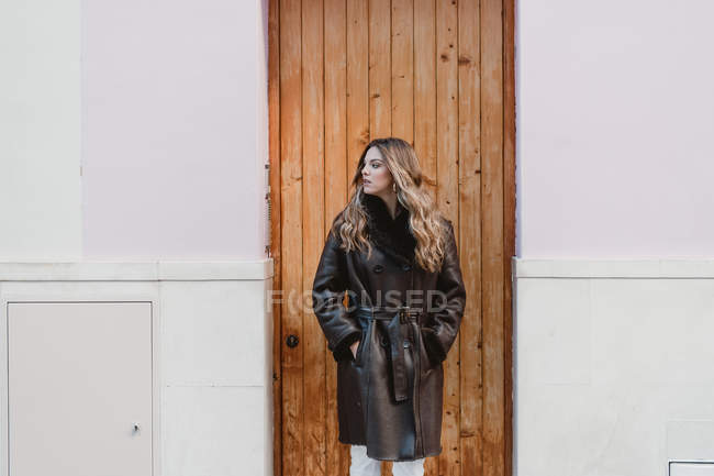 Stylische Frau im Vintage-Ledermantel steht neben Holztür auf der Straße — Stockfoto