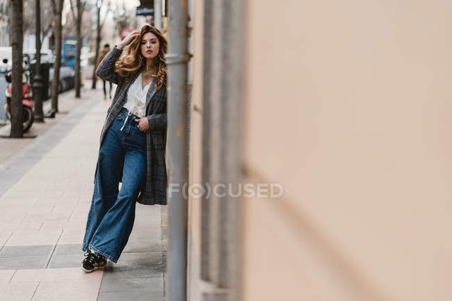 Stylische junge Frau lehnt auf der Straße an der Wand und blickt in die Kamera — Stockfoto
