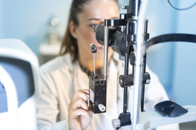 Trabajadora médica joven que usa microscopio en el lugar de trabajo con fondo borroso - foto de stock