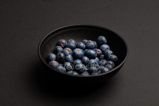 Bol de délicieux bleuets mûrs sur fond noir — Photo de stock