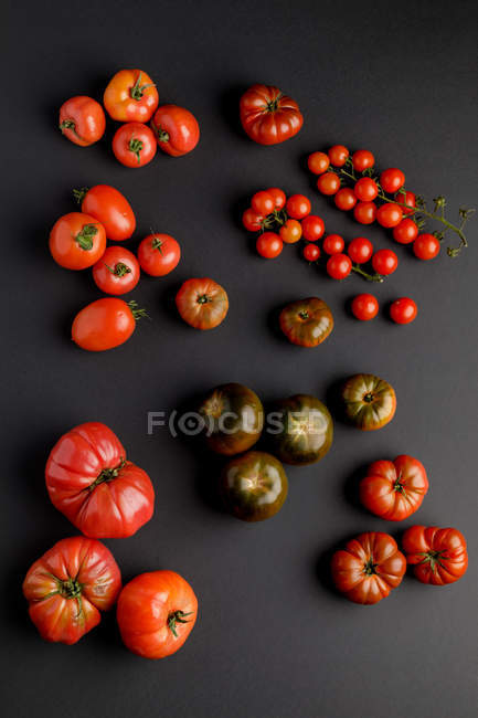 Pomodori freschi maturi assortiti sparsi sulla superficie nera — Foto stock