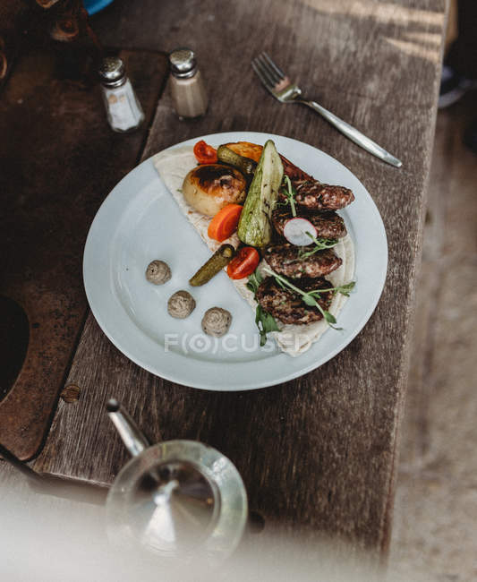 Arabic meat kebab plate with vegetables on plate on wooden table — Stock Photo