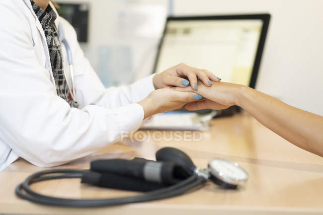 Tenant la main d'une femme médecin et d'un patient à table près d'un pulsomètre sur fond flou — Photo de stock