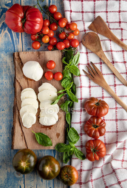 Свіжі помідори та сир моцарела з листям базиліка для салату на дерев'яній дошці та тканині — стокове фото