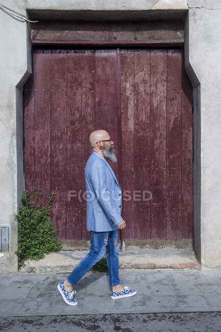Seitenansicht eines reifen trendigen bärtigen Hipsters, der im Freien gegen eine rote Vintage-Tür läuft — Stockfoto