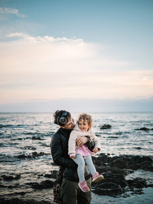 Scena carina di papà che tiene e abbraccia la sua piccola figlia in spiaggia in inverno — Foto stock