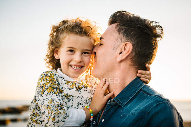 Мужчина средних лет с дочерью на берегу моря улыбаются и обнимают друг друга — стоковое фото