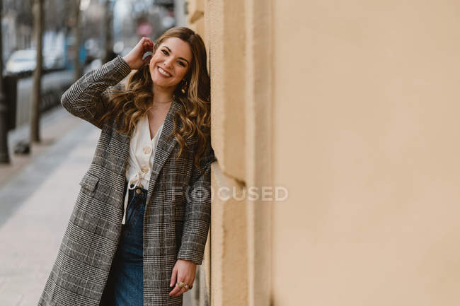 Felice giovane donna alla moda appoggiata al muro sulla strada — Foto stock