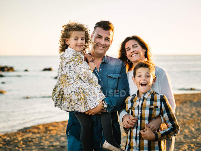 Чоловік середнього віку жінка з дітьми на морському березі посміхається і обіймає один одного — стокове фото