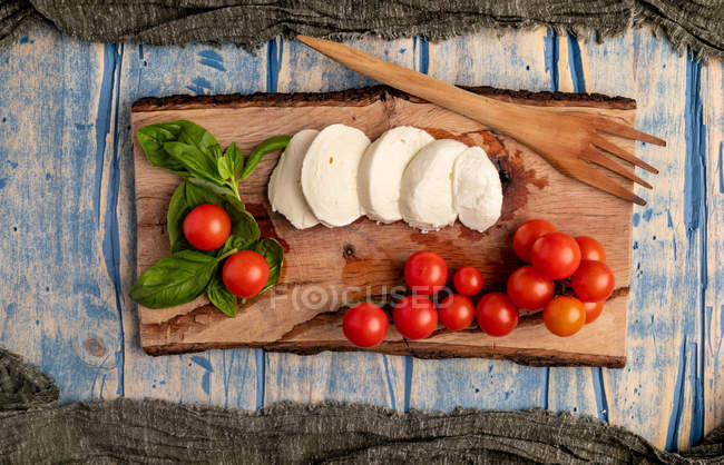 Tomates frescos e queijo mussarela com folhas de manjericão para salada caprese rústica em tábua de madeira — Fotografia de Stock