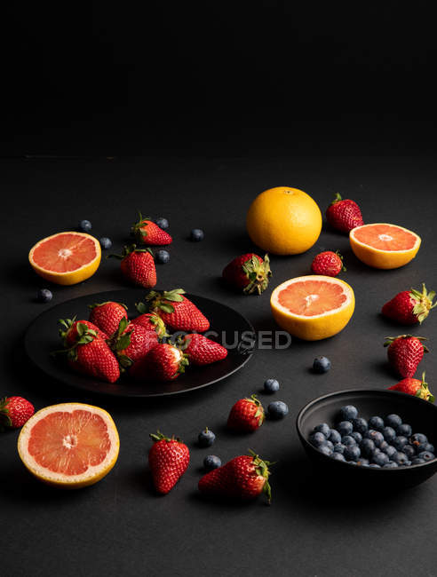 Verschiedene frische Früchte und Beeren auf schwarzem Hintergrund verstreut — Stockfoto