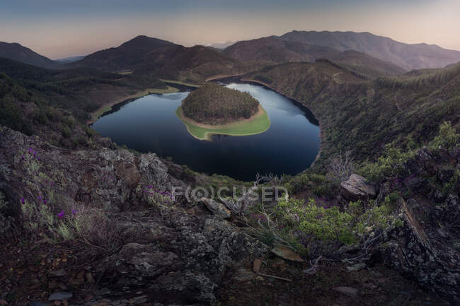 Aerial view of wooded island on smooth surface of lake in deserted undulating terrain — Stock Photo