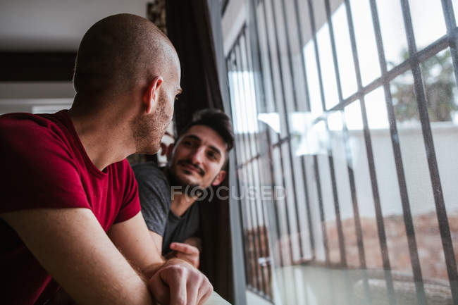 Romantic gay couple standing at window together — Stock Photo