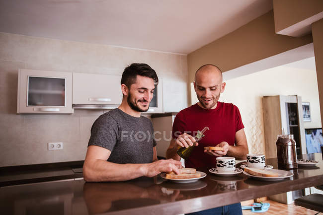 Alegre pareja gay teniendo desayuno en cocina en casa - foto de stock