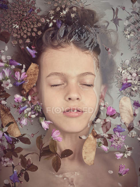 Сверху лицо ребенка в жидкости между свежими лепестками цветов — стоковое фото