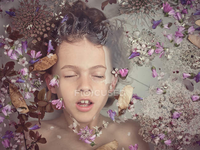 De arriba la persona del niño en el líquido entre los pétalos frescos de las flores - foto de stock