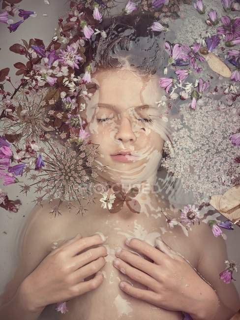 From above face of child in liquid between fresh petals of blooms — Stock Photo