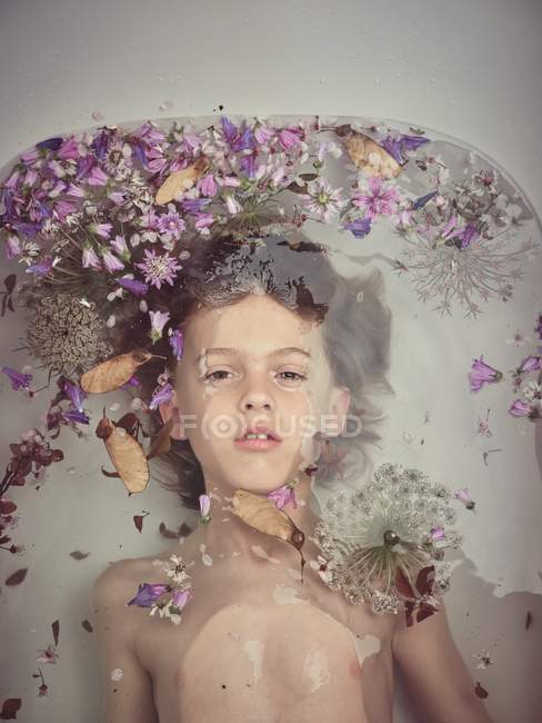 З висоти обличчя дитини в рідині між свіжими пелюстками квітів. — стокове фото