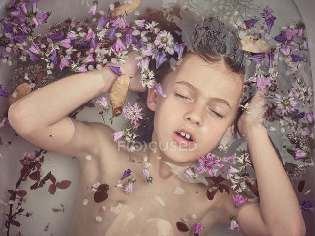 Сверху лицо ребенка в жидкости между свежими лепестками цветов — стоковое фото