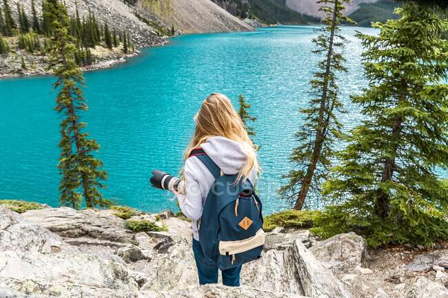 Vista posteriore del turista con zaino ripresa sulla macchina fotografica pittoresca vista della superficie dell'acqua e colline di pietra e cielo nuvoloso a Banff, Canada — Foto stock
