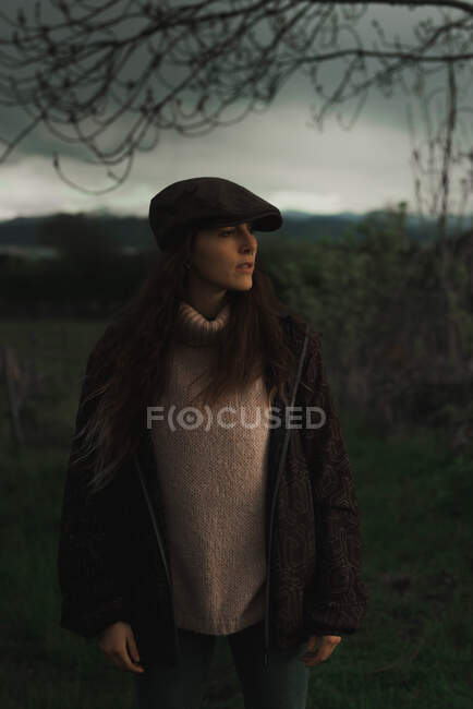 Jovem solitário bela mulher casual com cabelo castanho em casaco quente, suéter e chapéu em pé na floresta — Fotografia de Stock