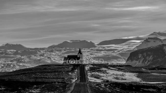 Церковное здание, расположенное рядом с грубой сельской дорогой против облачного неба в Исландии — стоковое фото