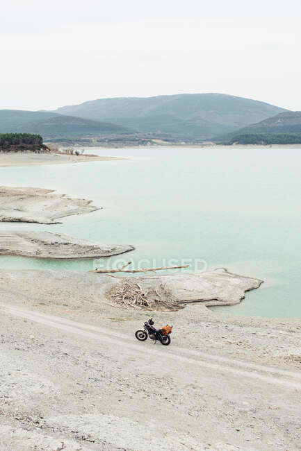 Moto estacionado en la carretera del campo en la orilla del lago tranquilo durante el viaje en la naturaleza - foto de stock