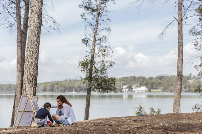 Madre e ragazzo pittura vicino lago — Foto stock