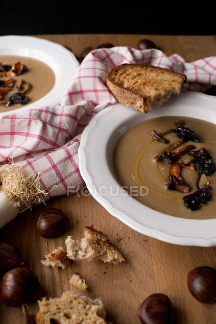 Assiettes de soupe aux châtaignes délicieuse aux champignons et serviette sur plateau en bois . — Photo de stock