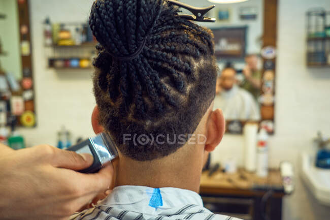 Vue de la récolte de derrière du coiffeur anonyme faisant une coupe de cheveux moderne avec un rasoir à un client afro-américain sans visage — Photo de stock