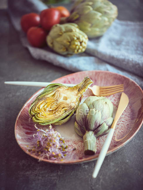 Knife and fork with halved fresh artichoke on pink ceramic plate — Stock Photo