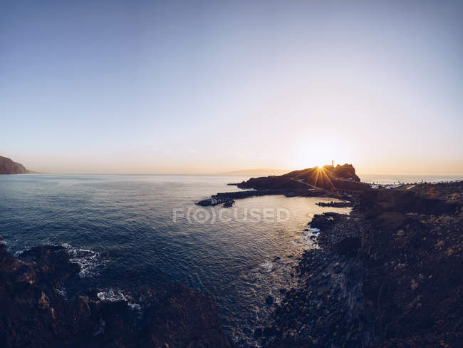 Pintoresco paisaje de brillante puesta de sol sobre la tranquila costa rocosa con olas onduladas, España - foto de stock