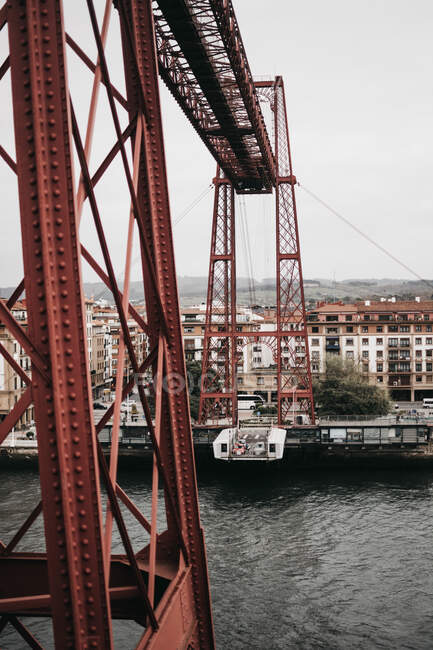 Вид на металлическое строение с гондолой над спокойной рекой в серый день в городе — стоковое фото