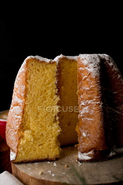 Cut fresh Italian Pandoro pastry on piece of wood against black background. — Stock Photo
