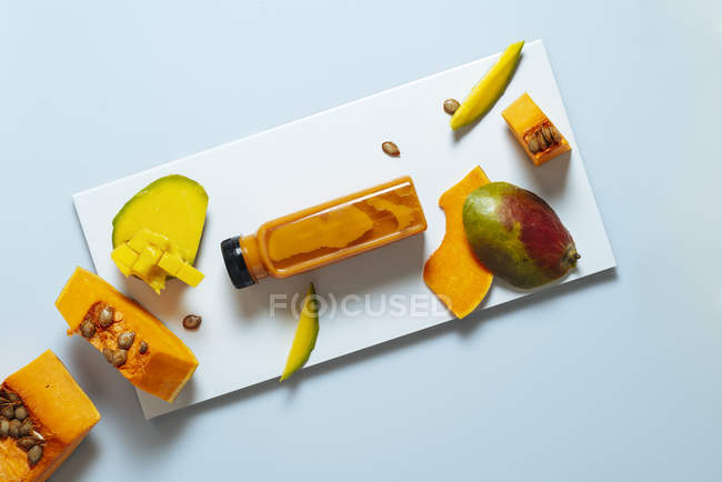 Botella de batido de mango y calabaza con ingredientes sobre fondo blanco - foto de stock