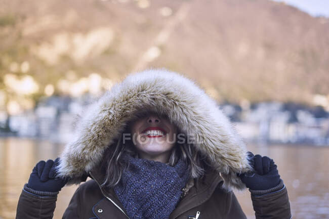 Cheerful woman in winter clothes covering eyes with a hood — Stock Photo
