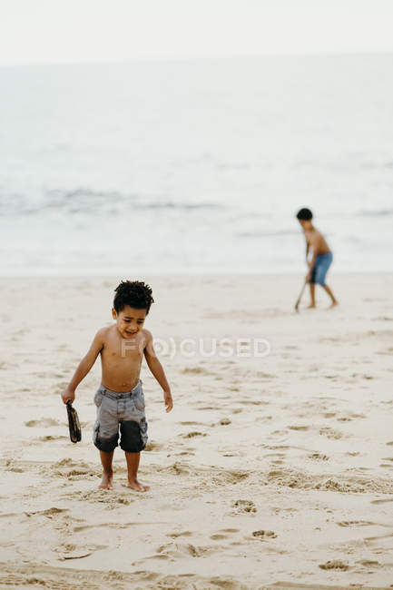 Afro-Américain garçon avec bâton jouant sur le rivage sablonneux près de la mer — Photo de stock