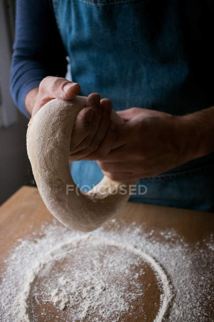 Unbekannter männlicher Koch formt frischen Teig mit Mehl, während er Rosca de Reyes über Holztisch in der Küche kocht. — Stockfoto
