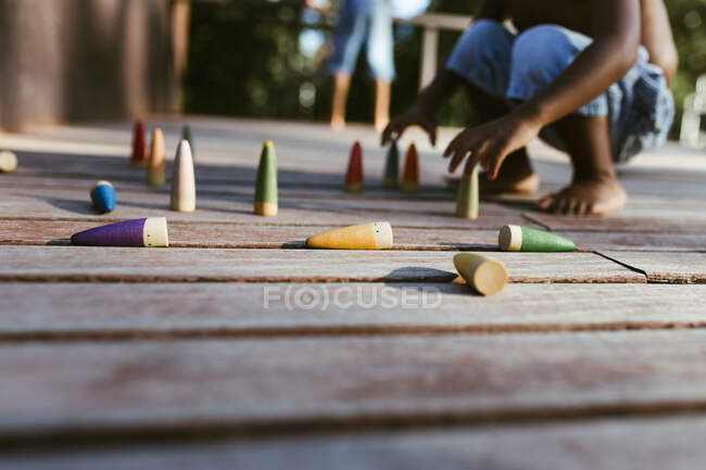 Menino afro-americano irreconhecível sem camisa sentado na superfície de madeira e brincando com cones coloridos no dia ensolarado — Fotografia de Stock