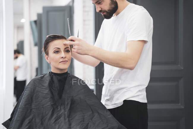 Peluquería corta el cabello de la mujer con tijeras - foto de stock