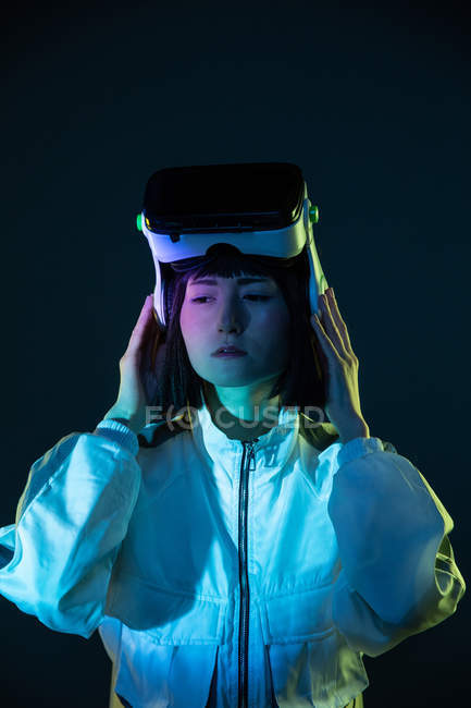 Mujer joven con gafas de realidad virtual mirando hacia otro lado en luz de neón - foto de stock
