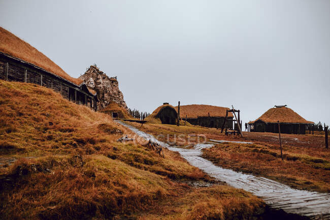 Cabañas antiguas ubicadas en la cima de la colina con hierba seca contra el cielo gris - foto de stock