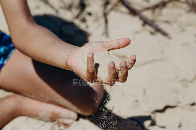 Очаровательный афроамериканец в повседневной одежде играет с сухим песком, проводя время во дворе в солнечный день — стоковое фото