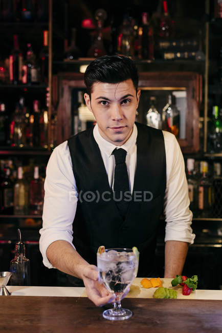 Jovem barman elegante trabalhando atrás de um balcão de bar misturando bebidas com frutas — Fotografia de Stock