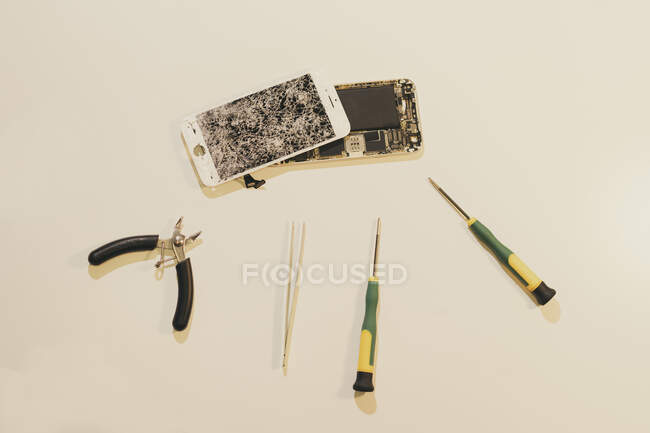 Apparecchiature di riparazione assortiti collocati su sfondo bianco vicino smartphone moderno con schermo danneggiato — Foto stock