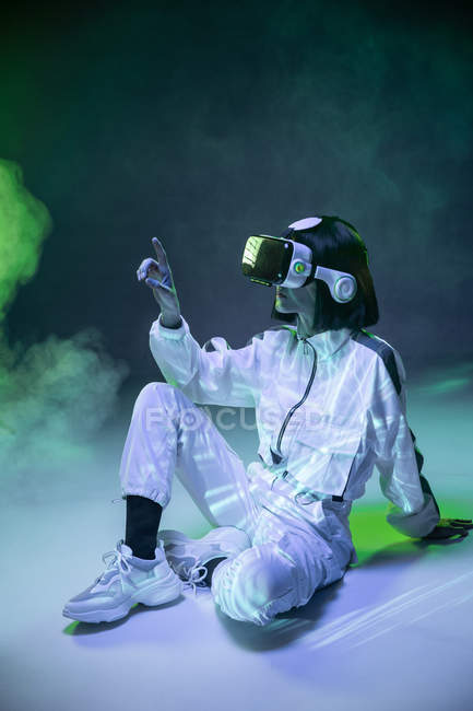 Mujer joven emocionada tocando el aire mientras tiene experiencia de realidad virtual en luz de neón - foto de stock