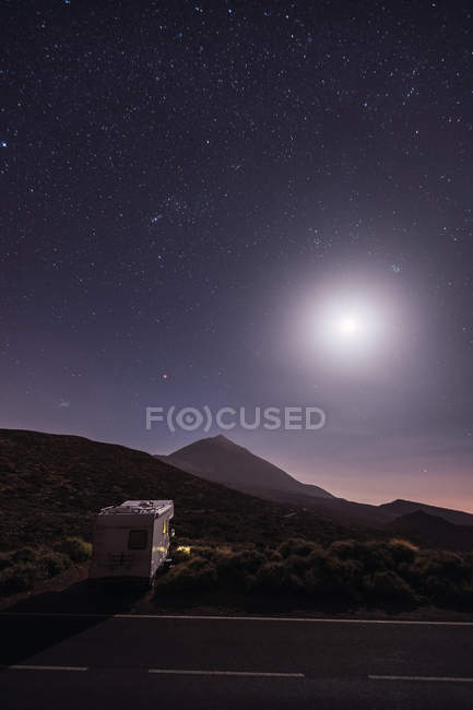 Caravana viajera estacionada cerca de la carretera en el desierto con luna brillante - foto de stock