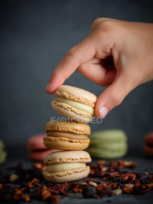 Mano di persona che prende macaron da una pila su sfondo grigio con frutta secca — Foto stock