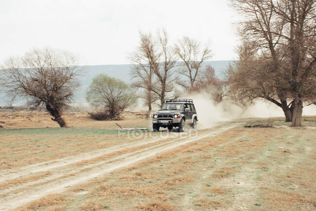 Off road car riding on dusty road near leafless trees during trip through countryside — Stock Photo